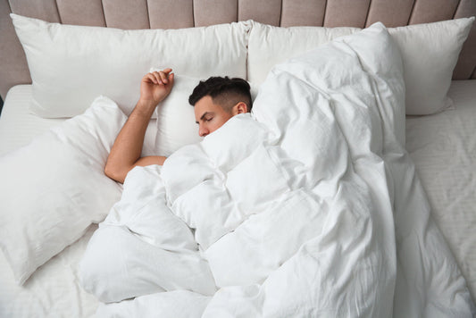 Handsome man sleeping under soft blanket in bed at home, above view