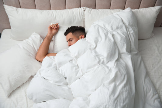 Handsome man sleeping under soft blanket in bed at home, above view